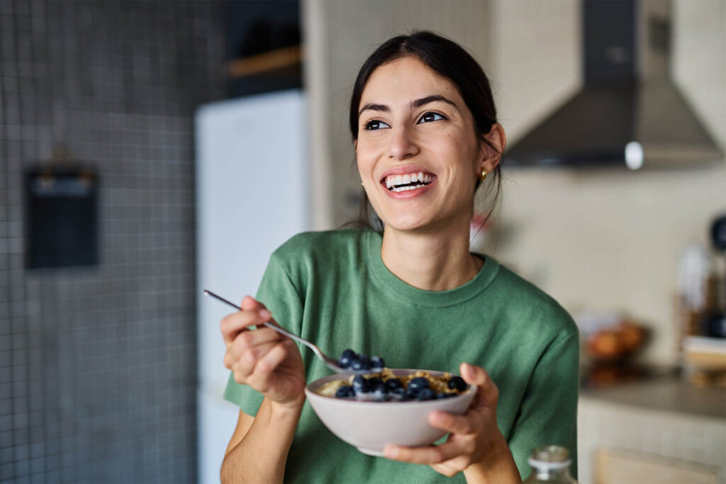 Portrait of a young woman preparing and eating breakfast, drinking juice in the kitchen at home